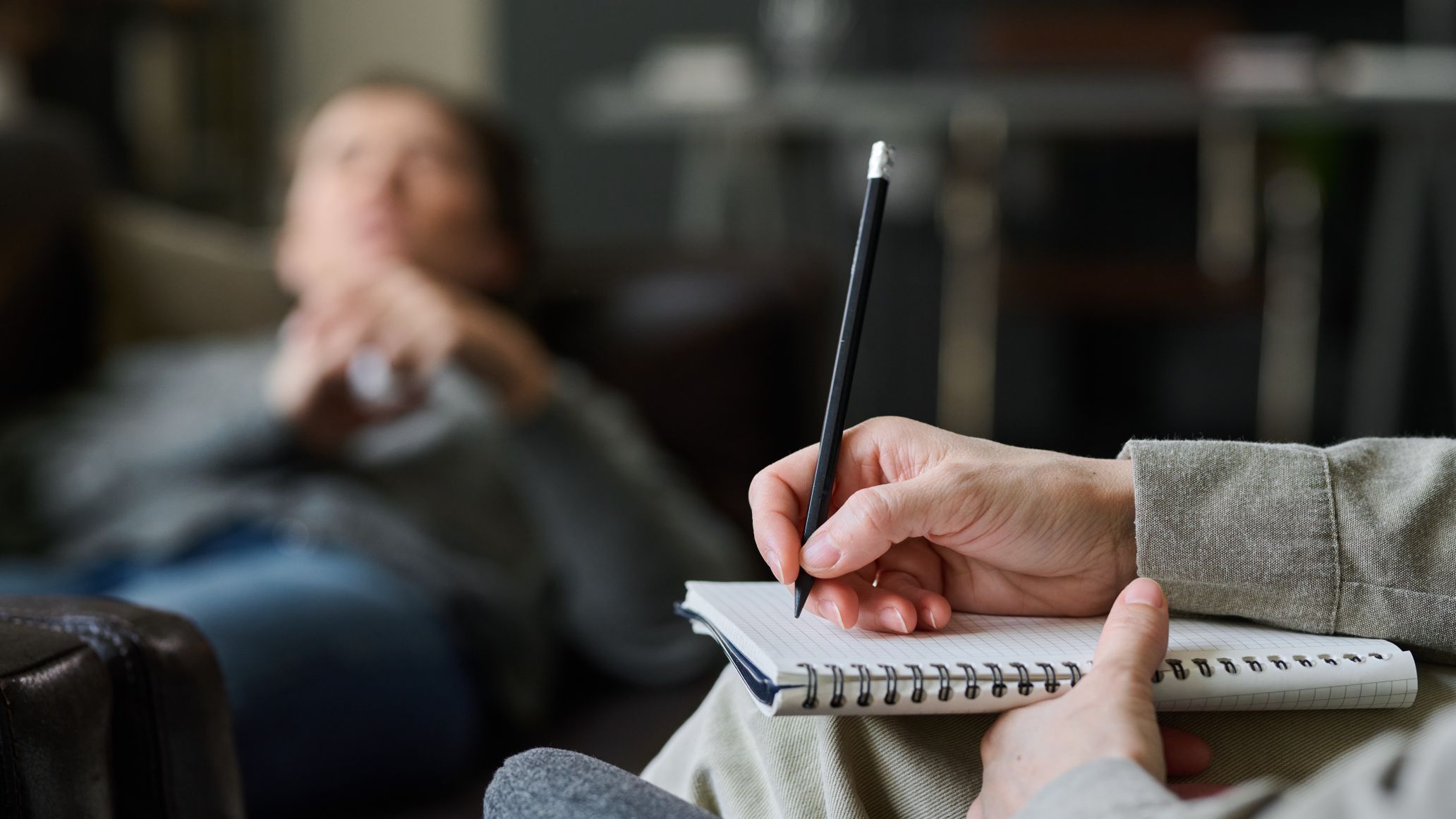 Therapist holding pen and notepad while patient sits in background with blurred face.